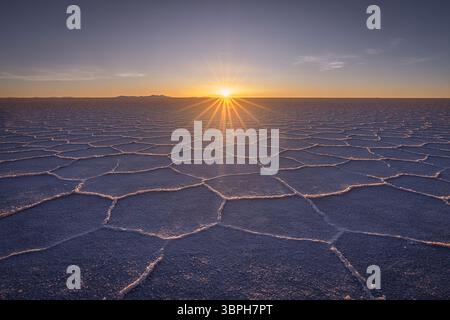 Vue du soleil se levant au-dessus de l'horizon éclairant les motifs hexagonaux sur les vastes salines de Salar de Uyuni, Uyuni, Departamento de Potosí, Bolivie. Banque D'Images