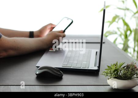 Gros plan d'une personne tapant sur son smartphone au bureau devant l'ordinateur portable Banque D'Images