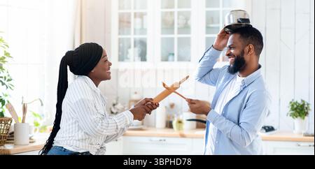 Joyeux couple noir s'amusant dans la cuisine, se battant ludique avec des ustensiles de cuisine Banque D'Images