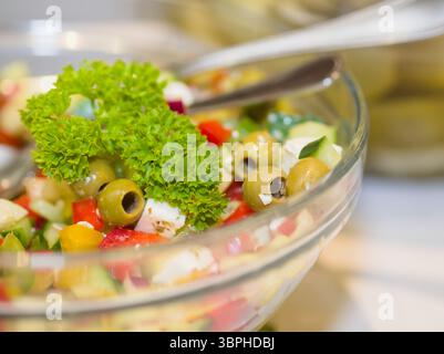 Gros plan d'une salade méditerranéenne fraîche avec des olives vertes éminentes, des légumes hachés colorés et une garniture de persil vibrante dans un verre clair Banque D'Images