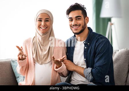 Bonne nouvelle. Couple musulman enceinte gai parlant à la caméra, faisant une annonce de grossesse Banque D'Images