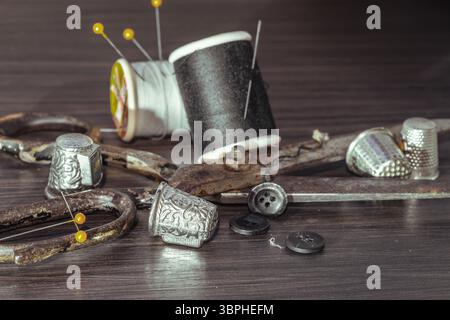 Aiguilles à coudre en argent, Thimbles, ciseaux en acier, ruban à mesurer, boutons noirs, bobines de fil noir et blanc, y compris épingles sur fond noir en bois. Banque D'Images