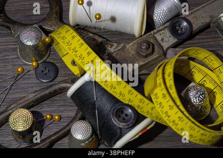 Aiguilles à coudre en argent, Thimbles, ciseaux en acier, ruban à mesurer, boutons noirs, bobines de fil noir et blanc, y compris épingles sur fond noir en bois. Banque D'Images