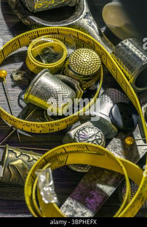 Aiguilles à coudre en argent, Thimbles, ciseaux en acier, ruban à mesurer, boutons noirs, bobines de fil noir et blanc, y compris épingles sur fond noir en bois. Banque D'Images