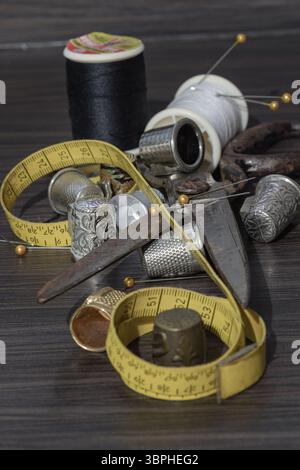 Aiguilles à coudre en argent, Thimbles, ciseaux en acier, ruban à mesurer, boutons noirs, bobines de fil noir et blanc, y compris épingles sur fond noir en bois. Banque D'Images