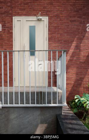 Porte crème moderne avec une élégante balustrade en métal gris contre un mur de briques rouges classique. Détail de l'architecture extérieure avec forte lumière du jour et des ombres. Banque D'Images