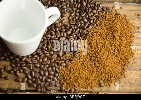 Montrant des grains de café plats de haut en bas se mélangeant dans le monticule de mouture sur la table en bois avec une tasse en céramique blanche Banque D'Images