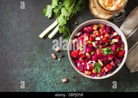 Concept de cuisine russe traditionnelle. Vinaigrette de salade de betteraves avec concombre mariné, haricots, carottes, petits pois, choucroute sur un comptoir foncé. Vue de dessus Banque D'Images