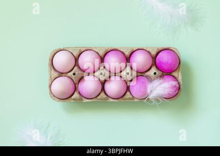 Concept minimal de Pâques. Éléments de Pâques, boîte en papier avec des œufs dans des couleurs roses sur fond vert pastel. Vue de dessus à plat Banque D'Images