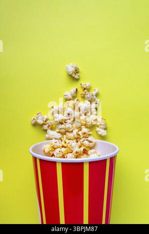 Pop-corn coulant d'un seau de papier rayé sur un fond jaune, copier l'espace Banque D'Images