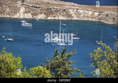 Une baie de baignade avec des voiliers et de l'eau turquoise à Lindos, un bastion touristique sur l'île grecque de Rhodes dans l'est de la Méditerrane Banque D'Images