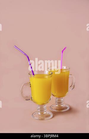 Deux verres avec jus d'orange et tubes à cocktail sur fond beige, espace copie Banque D'Images