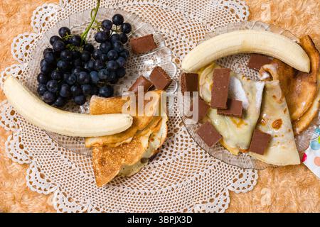 Crêpes aux fruits, chocolat et sucre sur une assiette en verre. Banque D'Images