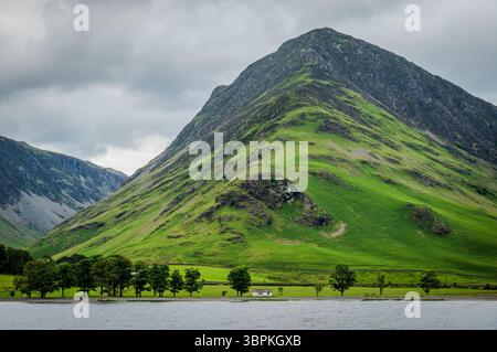 Un paysage d'été sombre avec une chute vertigineuse avec une petite cabane nichée à sa base, capturée par une journée nuageuse au lac Buttermere Banque D'Images