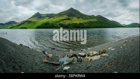 La vue panoramique depuis la rive du lac Buttermere montre des rochers dispersés le long de la plage de galets, des vagues balayées par le vent sur le lac Banque D'Images