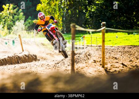 Un pilote de motocross dans un équipement lumineux navigue sur une piste de terre sablonneuse lors d'une course de moto tout-terrain, mettant en valeur l'action dynamique et la maniabilité qualifiée Banque D'Images