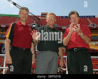 24 avril 2004, Landover, Maryland, États-Unis : près de 44 000 fans de Redskin se sont présentés au FedEx Field à Landover, Maryland pour acheter des souvenirs, grignoter des collations à prix réduit, troder sur le terrain des Redskins et regarder la draft 2004 de la NFL sur les Jumbotrons le 24 avril 2004. Après que les Redskins eurent fait leur premier tour, l'entraîneur-chef Joe Gibbs, au centre, le coordinateur défensif Gregg Williams, à gauche, et le coordinateur offensif Joe Bugel, à droite, sont arrivés pour discuter avec les fans et répondre aux questions. Les entraîneurs Williams, Gibbs et Bugel font leurs adieux à la foule en quittant le terrain. Derrière eux, on peut voir t Banque D'Images