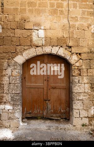 L'ancienne porte double en bois usée, située dans un mur de pierre rustique, affiche son charme historique et sa décadence architecturale. L'ancienne porte située à l'intérieur du h. Banque D'Images