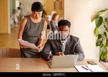 Homme d'affaires lisant l'e-mail sur ordinateur portable tandis que professionnel féminin analysant le rapport tout en se tenant à côté de lui au bureau Banque D'Images