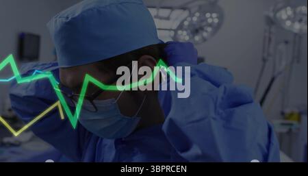 Chirurgien adulte portant des gants de réglage bleus, coiffe sous les lumières chirurgicales dans LE BLOC OPÉRATOIRE, avec recouvrement ECG Banque D'Images