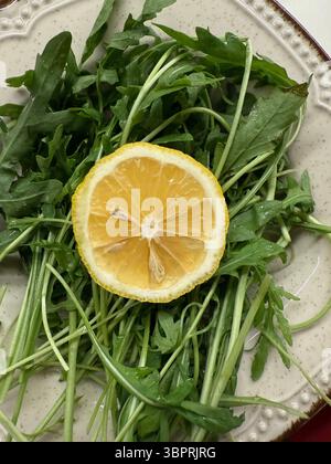 Cette image montre une tranche de citron positionnée sur des feuilles fraîches de roquette (roquette), disposées sur une plaque de céramique. La photo est prise de haut en bas Banque D'Images