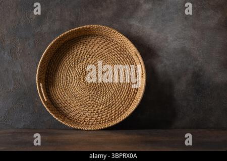 Panier rond en osier tissé, plateau ou support de plaque sur fond brun. Fait à la main par des artisans locaux au sri lanka vaisselle traditionnelle. Banque D'Images