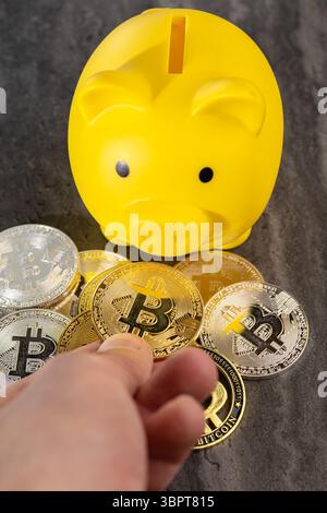 Un bitcoin doré est maintenu vers une tirelire jaune sur une surface réfléchissante, symbolisant l’investissement en crypto-monnaie et l’épargne sur les actifs numériques, contras Banque D'Images