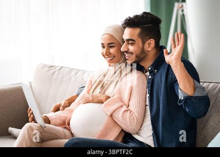 Joyeux futurs conjoints musulmans faisant des appels vidéo avec la tablette numérique À la maison Banque D'Images