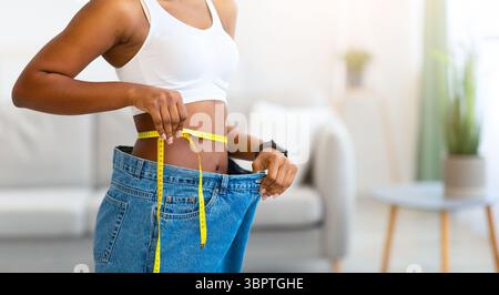 Happy Black Lady montrant de grands jeans mesurant la taille mince à l'intérieur Banque D'Images