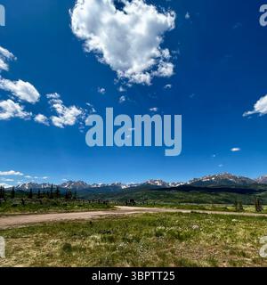 Champ vert ouvert avec clôture en bois rustique menant aux montagnes enneigées lointaines Banque D'Images