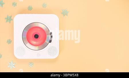 Un lecteur CD blanc moderne est vu d'en haut, avec un CD à l'intérieur. Il s entouré de délicates décorations de flocon de neige sur un fond jaune pastel doux, Banque D'Images
