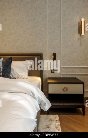 Gros plan d'une table de chevet élégante dans une chambre de luxe. Dispose d'une poignée en laiton, cadre en bois foncé, et est fixé contre un mur avec moulure classique. Banque D'Images