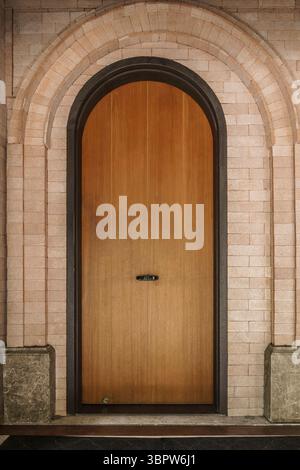 Porte en bois voûtée élégante placée à l'intérieur d'une arche murale de briques. Design architectural classique avec une poignée moderne et minimaliste. Symbole d'entrée ou opportun Banque D'Images