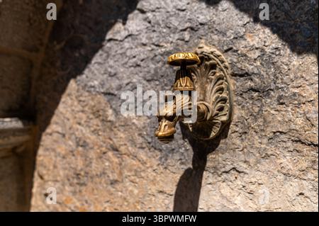 Bec d'eau en laiton avec motif animal est monté sur un mur de pierre texturé à l'extérieur. Banque D'Images