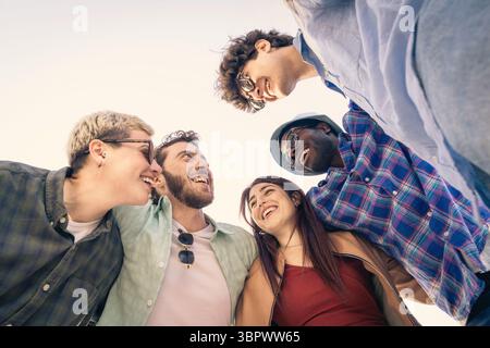 Un groupe multiethnique diversifié de jeunes amis blottis dans un cercle et se regardant avec un rire authentique, symbolisant un lien fort, complice Banque D'Images