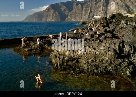 Les gens nagent dans des piscines côtières naturelles avec les montagnes Los Gigantes et les falaises à distance, Charco de Isla Cangrejo, Tenerife, îles Canaries, Espagne Banque D'Images