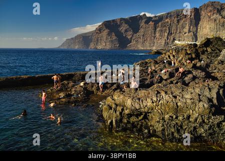Les gens nagent dans des piscines côtières naturelles avec les montagnes Los Gigantes et les falaises à distance, Charco de Isla Cangrejo, Tenerife, îles Canaries, Espagne Banque D'Images