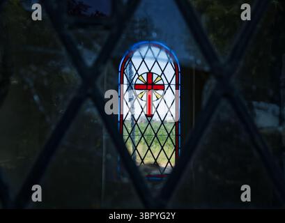 Lumière douce du soleil traversant la croix de vitrail rouge, projetant une lueur chaleureuse et éthérée à l'intérieur de l'église historique Banque D'Images