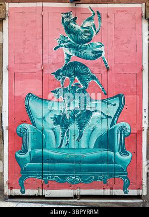 Art de rue coloré sur une porte en bois à Barcelone avec des chats turquoise ludiques tombant sur un fauteuil sarcelle orné sur un fond rose. Banque D'Images