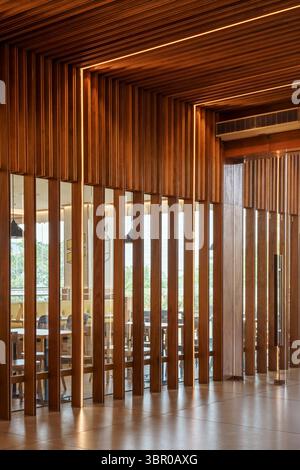 L'intérieur moderne du restaurant comprend un mur de séparation à lamelles en bois avec miroir intégré et un éclairage LED chaud. Banque D'Images
