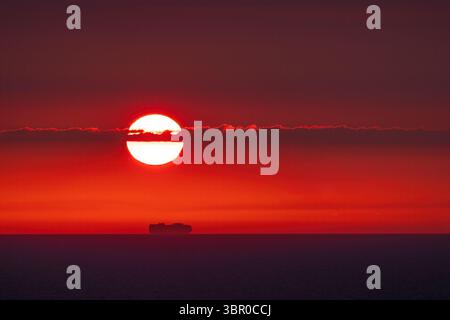 Superbe coucher de soleil sur la mer près du Danemark, capturé depuis un bateau de croisière. Les éoliennes dessinent l'horizon sous un ciel rouge et orange éclatant. Banque D'Images