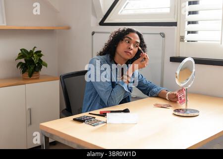 Personne afro-américaine assise au bureau appliquant le maquillage des sourcils avec la palette rose, espace de copie. Beauté, toilettage, soins personnels, vanité, cosmétique, auto Banque D'Images