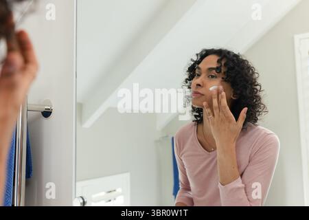 Afro-américain individuel appliquant la crème de soin de la peau du pot à la vanité de plafond incliné, espace de copie. Soin de la peau, soin de soi, beauté, réflexion, minimaliste Banque D'Images