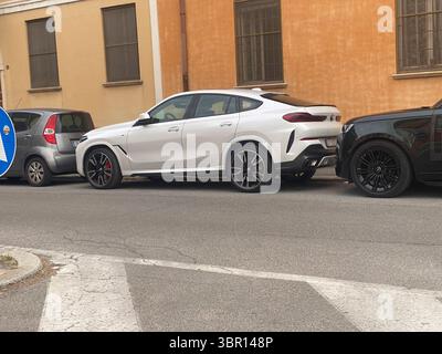 Cremona, Italie 8 juin 2025 Blanc BMW X6 M compétition avec jantes noires et rouges garé près d'un mur orange dans une rue de la ville, mettant en valeur son sport et Banque D'Images