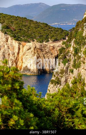 Une crique isolée encadrée par des falaises accidentées et ensoleillées et une végétation luxuriante, révélant les eaux bleues profondes de la mer Ionienne. Banque D'Images