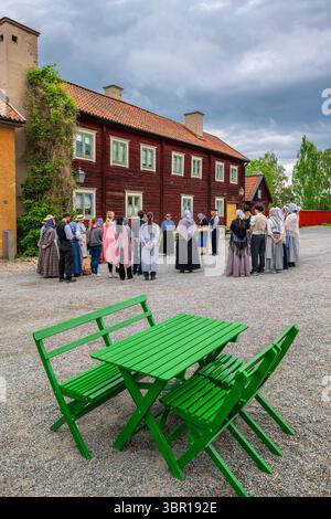 Sodertalje, Suède - 6 juin 2025 : un groupe de personnes habillées en tenue traditionnelle dans le musée en plein air Terekallberget se sont rassemblées à l'extérieur d'un bâtiment rustique Banque D'Images