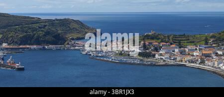 Vue aérienne de la ville animée nichée entre les collines verdoyantes et la mer Azur, avec un port animé rempli de bateaux, Horta, Açores, Portugal. Banque D'Images