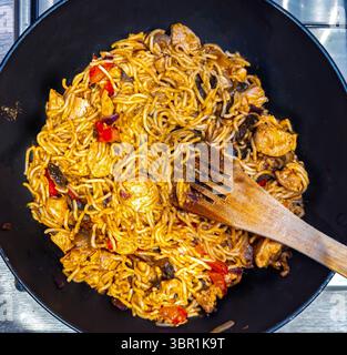 Nouilles sautées avec poulet et légumes cuisinés dans un wok ou une poêle avec une spatule en bois, montrant un appétissant plat de cuisine asiatique Banque D'Images