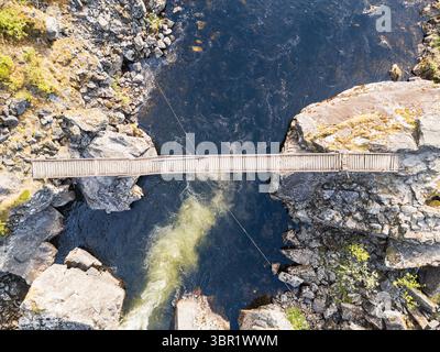 Une vue aérienne d'un dangereux passage sur un pont suspendu mouvementé au-dessus d'une rivière de montagne barattant. Un concept d'aventure, de tourisme et de nature sauvage Banque D'Images