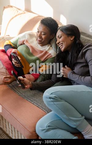 Diverses amies féminines assises sur un canapé rosé-corail dans le salon, partageant le contenu du smartphone. Amitié, décontracté, contemporain, style de vie, confortable, donc Banque D'Images
